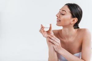 Young woman in underwear lying down in the studio against white background with beauty cream in hands photo