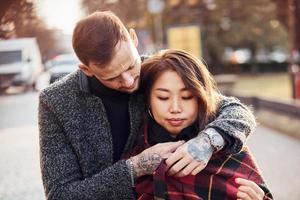 Happy multiracial couple warming up by red plaid together outdoors in the city photo