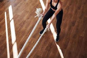 On the floor illuminated by light beams. Young sporty woman in sportswear doing fitness by using knots photo