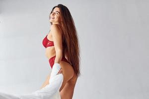 mujer en ropa interior roja que cubre su cuerpo con una toalla en el estudio con fondo blanco foto