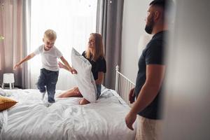 Young married couple with their young son have leisure together in bedroom at daytime photo