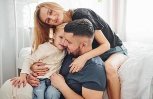 Young married couple with their young son have leisure together in bedroom at daytime photo