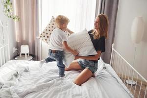 Mother playing pillow fight with her son in bedroom at daytime photo