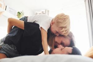 joven pareja casada con su hijo pequeño acostado en la cama y divertirse juntos en el dormitorio durante el día foto