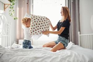 Mother playing pillow fight with her son in bedroom at daytime photo