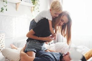 Young married couple with their young son have leisure together in bedroom at daytime photo