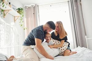 Young married couple with their young son have leisure together in bedroom at daytime photo