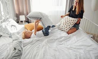 Mother playing pillow fight with her son in bedroom at daytime photo