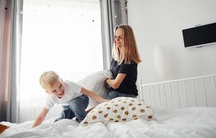 Mother playing pillow fight with her son in bedroom at daytime photo