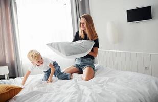 madre jugando pelea de almohadas con su hijo en el dormitorio durante el día foto