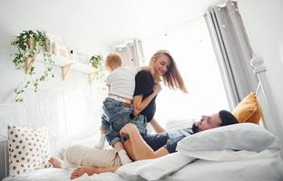 joven pareja casada con su hijo pequeño acostado en la cama y divertirse juntos en el dormitorio durante el día foto