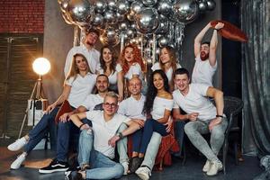 jóvenes positivos sentados y celebrando el año nuevo en una habitación decorada de navidad con globos juntos foto