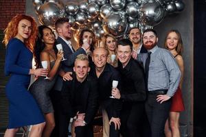 People in elegant clothes with drinks in hands standing together and celebrating New Year holidays in christmas decorated room photo