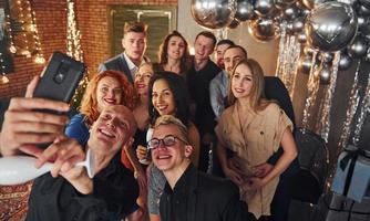 hombre tomando selfie de sus amigos que están parados en una habitación decorada con navidad y celebrando las vacaciones de año nuevo foto