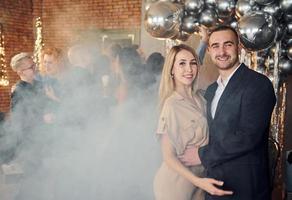 elegante pareja joven de pie junto a sus amigos en una habitación decorada con navidad y celebrando el año nuevo foto