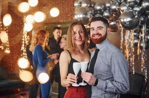 joven barbudo con su novia parados juntos contra sus amigos en una habitación decorada de navidad y celebrando el año nuevo foto