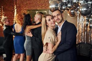 elegante pareja joven de pie junto a sus amigos en una habitación decorada con navidad y celebrando el año nuevo foto