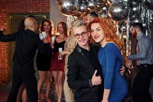 Young man with redhead woman is together against their friends in christmas decorated room and celebrating New Year photo