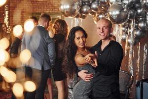 Young couple dancing against their friends in christmas decorated room and celebrating New Year photo