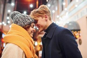 Cute couple in warm clothes is on christmas decorated street smiling and have fun photo