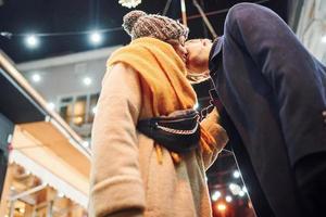 Young couple in warm clothes kissing on christmas decorated street photo