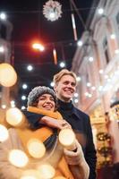 Positive young couple in warm clothes embracing each other on christmas decorated street photo