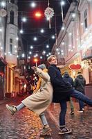 Cute couple in warm clothes is on christmas decorated street smiling and have fun photo