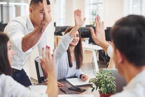 Giving high five to each other. Young business people celebrating success in the modern office photo