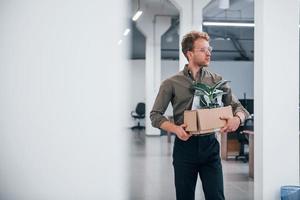 Office worker in formal wear walking with box with green plant inside of it photo