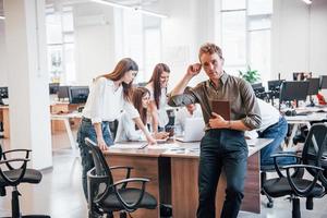 joven empleado con ropa formal de pie en la oficina. grupo de personas que trabajan detrás foto