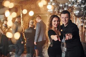 Young couple standing together against their friends in christmas decorated room and celebrating New Year photo