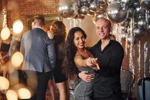 pareja joven bailando contra sus amigos en una habitación decorada con navidad y celebrando el año nuevo foto