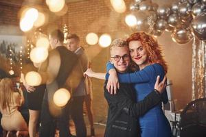 Young couple standing together against their friends in christmas decorated room and celebrating New Year photo