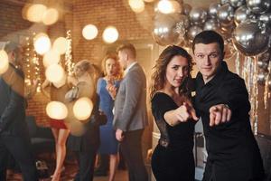 Young couple standing together against their friends in christmas decorated room and celebrating New Year photo