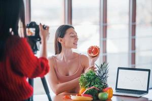 modelo de fitness tiene una sesión de fotos de una fotógrafa en el interior junto a la mesa con comida saludable