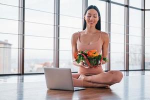 Sportive woman sitting on the table with laptop and healthy food photo