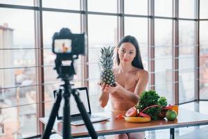 Young fitness vlogger doing video indoors by sitting near table with healthy food photo