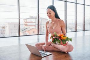 Sportive woman sitting on the table with laptop and healthy food photo