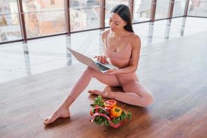 Sportive woman sitting on the table with laptop and healthy food photo