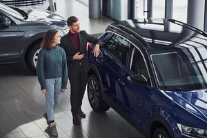 vendedor profesional que ayuda a la joven a elegir un nuevo automóvil moderno en el interior foto