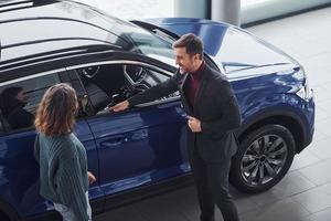 Professional salesman assisting young girl by choosing new modern automobile indoors photo