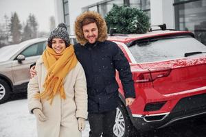 Young couple standing near car with tree on the top. Together outdoors at winter time photo