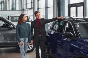 Professional salesman assisting young girl by choosing new modern automobile indoors photo