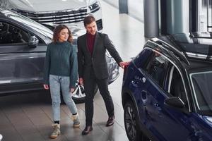 Professional salesman assisting young girl by choosing new modern automobile indoors photo