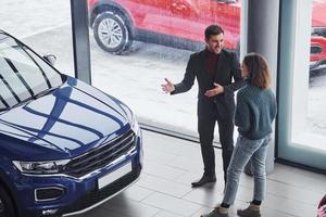 vendedor profesional que ayuda a la joven a elegir un nuevo automóvil moderno en el interior foto