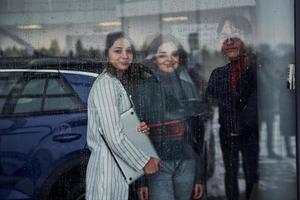 amigos parados detrás de un vidrio en un día lluvioso. la chica sostiene la computadora portátil en las manos foto