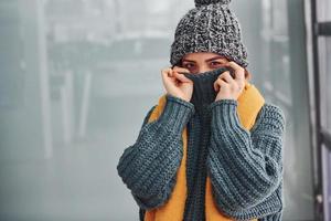 Beautiful cheerful girl in yellow scarf and in warm clothes standing indoors against background with reflections photo