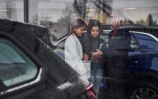 Friends standing behind glass at rainy day. Girl holds laptop in hands photo
