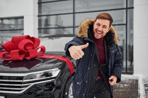 feliz propietario de un nuevo camión moderno parado al aire libre y sonriendo. longitud de regalo rojo en el automóvil foto