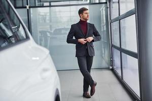 Young business man in luxury suit and formal clothes is indoors near the car photo